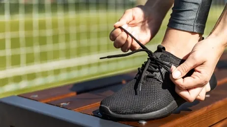 ผู้หญิงยืนผูกเชือกรองเท้าบนม้านั่ง